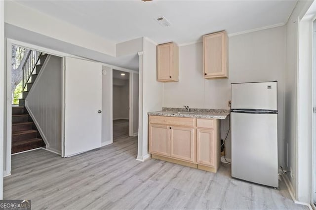 kitchen with light hardwood / wood-style flooring, ornamental molding, sink, white refrigerator, and light brown cabinetry