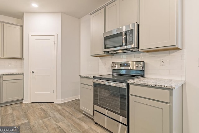 kitchen featuring stainless steel appliances, baseboards, backsplash, light stone countertops, and light wood finished floors