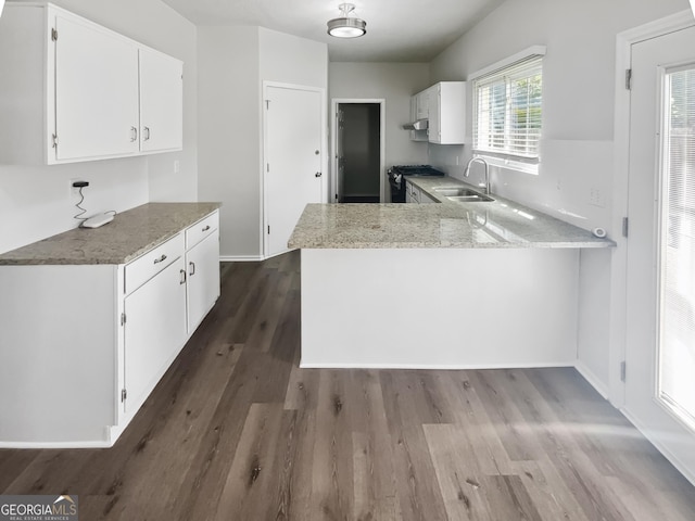 kitchen with a sink, gas range oven, a peninsula, and light stone counters