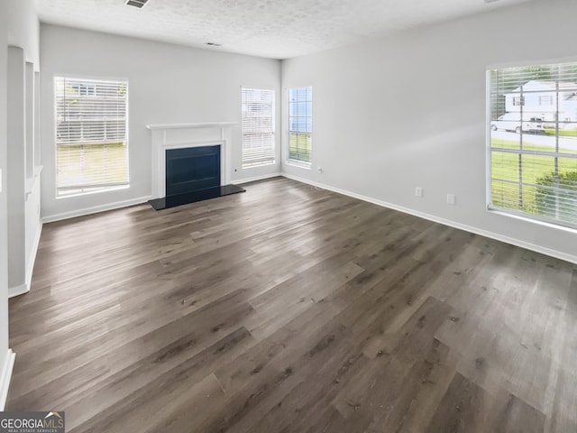 unfurnished living room featuring dark wood-style floors, baseboards, a fireplace with raised hearth, and a textured ceiling