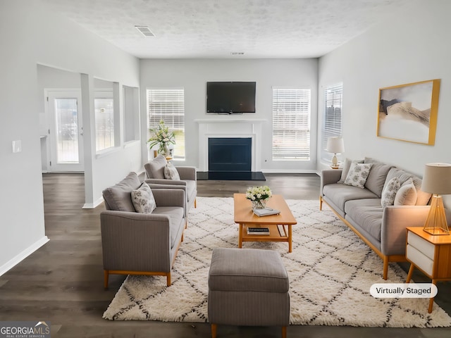 living room featuring baseboards, a fireplace with raised hearth, a textured ceiling, and wood finished floors