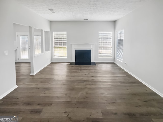 unfurnished living room with a textured ceiling, a fireplace with raised hearth, dark wood-type flooring, and baseboards