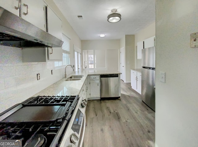 kitchen with appliances with stainless steel finishes, decorative backsplash, white cabinets, light wood-type flooring, and sink