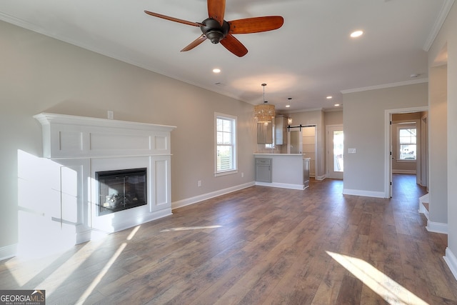 unfurnished living room with a barn door, ceiling fan, dark wood-type flooring, and ornamental molding