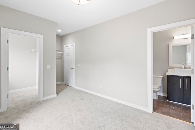 unfurnished bedroom with sink, a closet, a spacious closet, light carpet, and ensuite bath