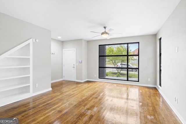 unfurnished room with wood-type flooring, built in shelves, and ceiling fan