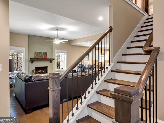 stairway featuring hardwood / wood-style floors, a large fireplace, and ceiling fan