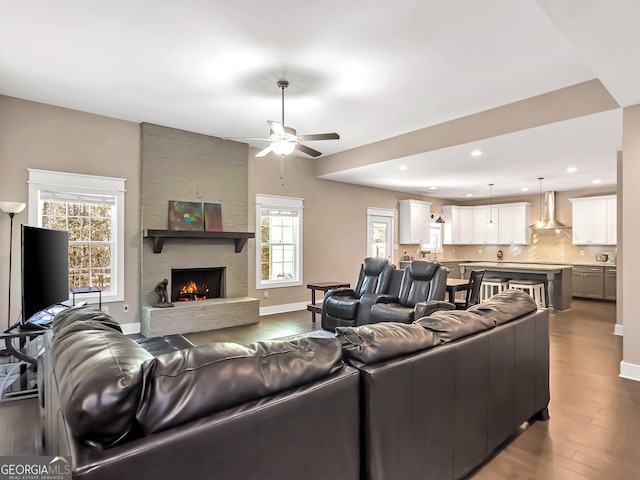 living room featuring wood-type flooring, a stone fireplace, ceiling fan, and a healthy amount of sunlight