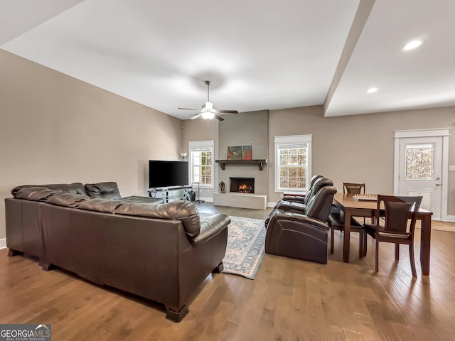 living room featuring ceiling fan, wood-type flooring, and a brick fireplace