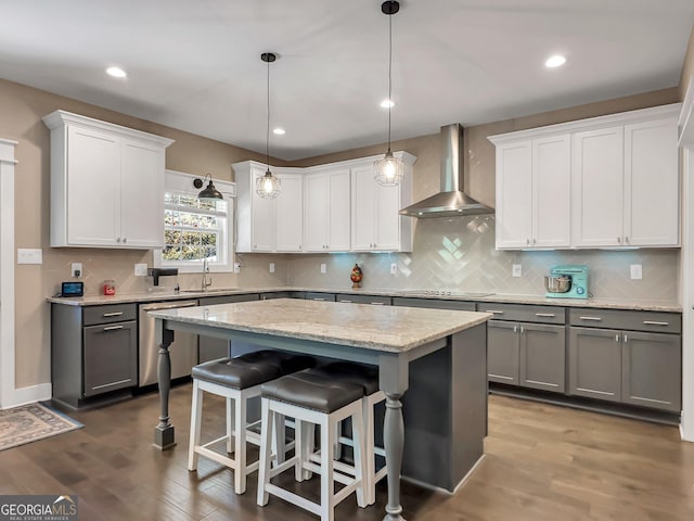 kitchen featuring stainless steel dishwasher, a kitchen island, wood-type flooring, and wall chimney range hood