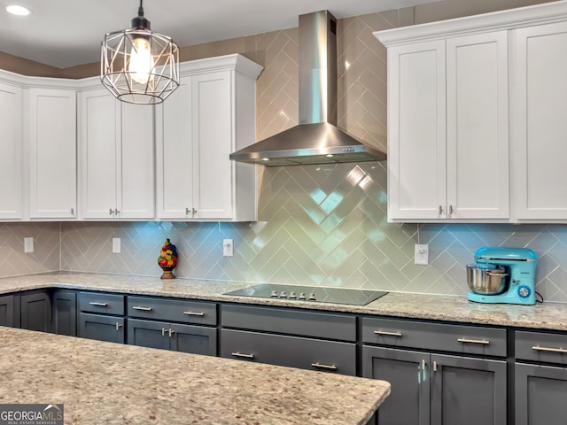 kitchen with wall chimney exhaust hood, light stone counters, decorative light fixtures, decorative backsplash, and white cabinets