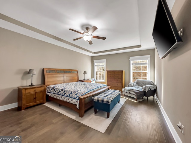 bedroom with dark hardwood / wood-style flooring, a raised ceiling, and ceiling fan