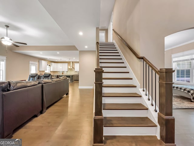 staircase with wood-type flooring, a wealth of natural light, ornamental molding, and ceiling fan