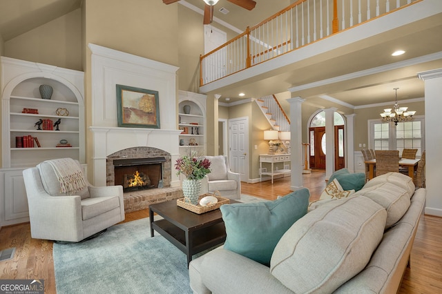 living area with built in shelves, decorative columns, a high ceiling, a brick fireplace, and wood finished floors