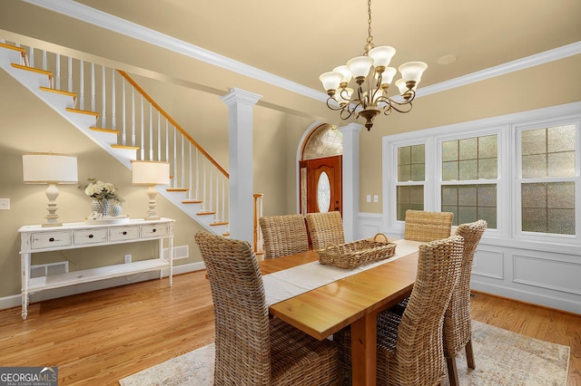 dining area with decorative columns, stairway, wood finished floors, and ornamental molding