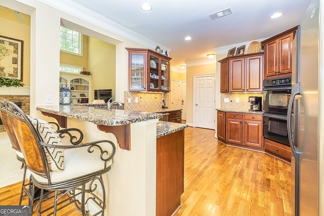 kitchen with light wood-type flooring, ornamental molding, kitchen peninsula, a breakfast bar, and light stone countertops