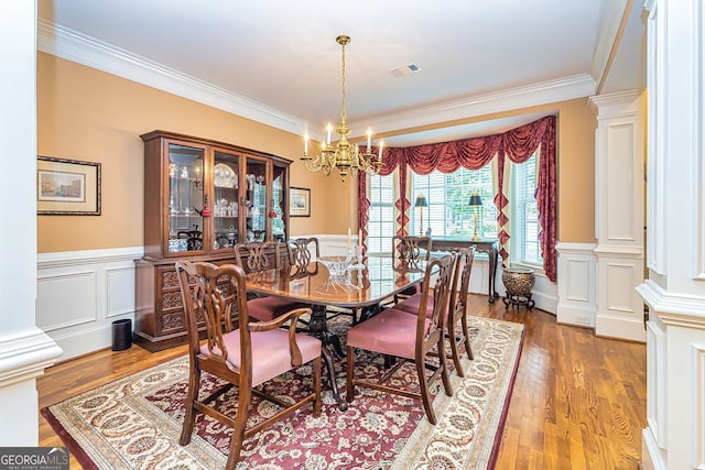 dining space with wood-type flooring, ornamental molding, a notable chandelier, and decorative columns