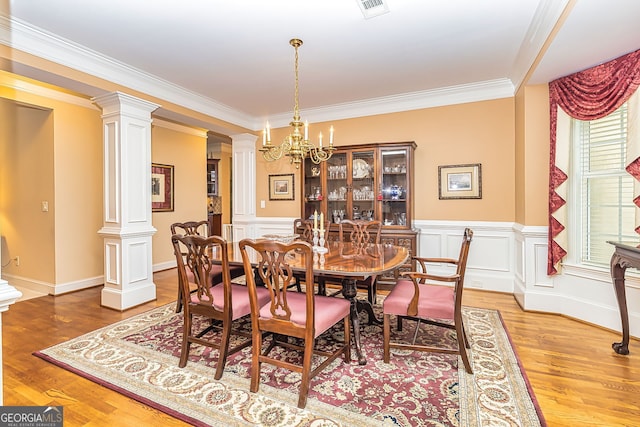 dining area with ornamental molding, wood-type flooring, a chandelier, and decorative columns