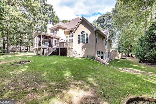 back of house featuring a wooden deck, a sunroom, an outdoor fire pit, and a yard