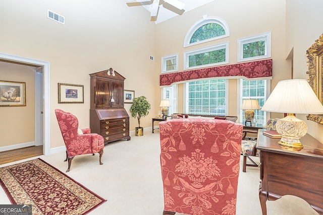 living room with ceiling fan, light colored carpet, a towering ceiling, and a wealth of natural light