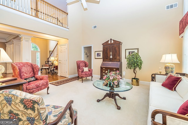 living room featuring ceiling fan, ornate columns, ornamental molding, a towering ceiling, and hardwood / wood-style floors