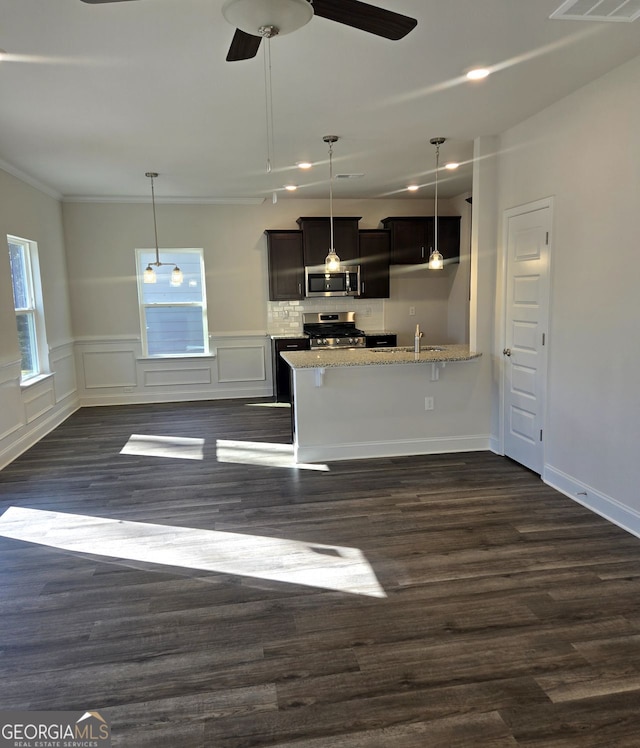 kitchen with appliances with stainless steel finishes, dark wood-type flooring, decorative light fixtures, and light stone countertops