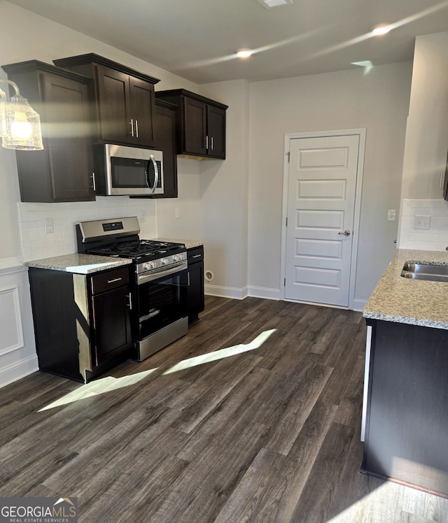 kitchen with light stone counters, dark wood-style flooring, a sink, appliances with stainless steel finishes, and decorative backsplash