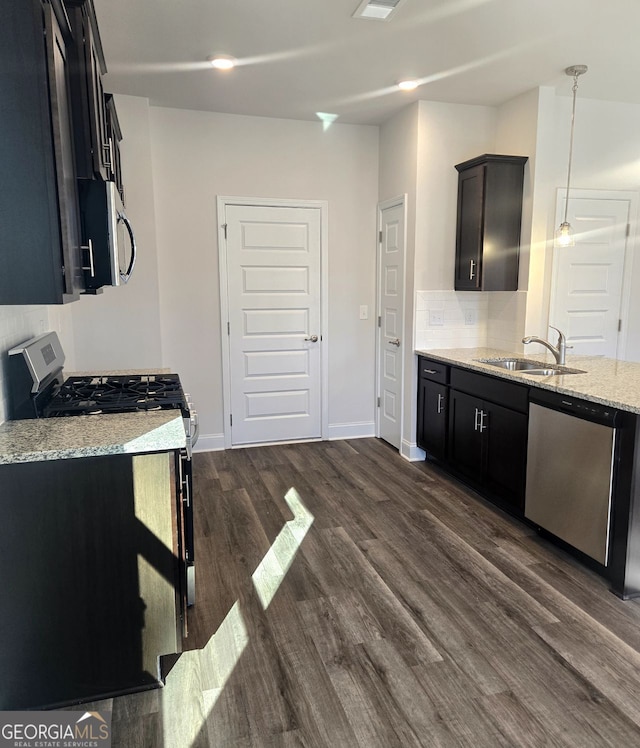 kitchen with light stone counters, decorative light fixtures, stainless steel appliances, dark cabinetry, and a sink