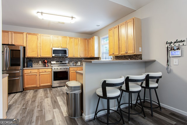 kitchen featuring kitchen peninsula, stainless steel appliances, a breakfast bar, light wood-type flooring, and decorative backsplash