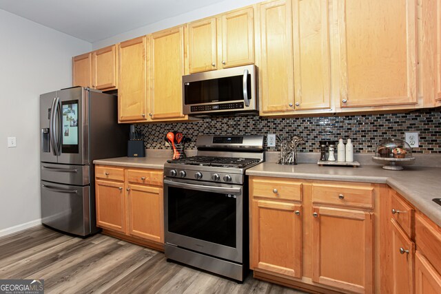 kitchen with appliances with stainless steel finishes, wood-type flooring, and decorative backsplash