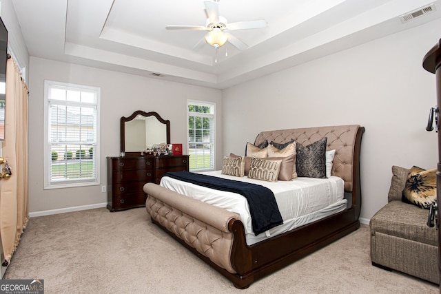 bedroom featuring ceiling fan, light colored carpet, a tray ceiling, and multiple windows