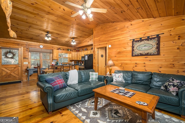 living room with light wood-type flooring, wood walls, ceiling fan, and vaulted ceiling