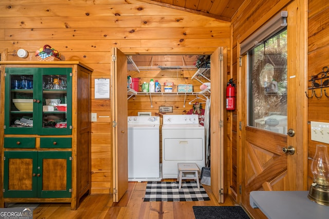 clothes washing area with wooden ceiling, washer and clothes dryer, wooden walls, and light hardwood / wood-style flooring