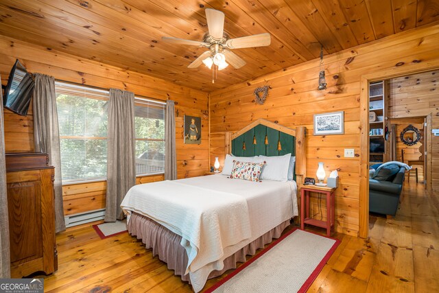 bedroom with a baseboard heating unit, light wood-type flooring, wooden walls, ceiling fan, and wooden ceiling