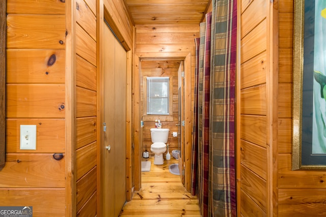 hall with light wood-type flooring, wooden ceiling, and wooden walls