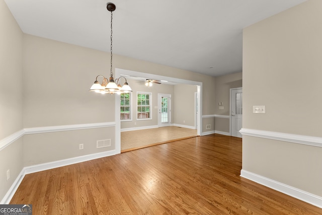 spare room with ceiling fan with notable chandelier and wood-type flooring