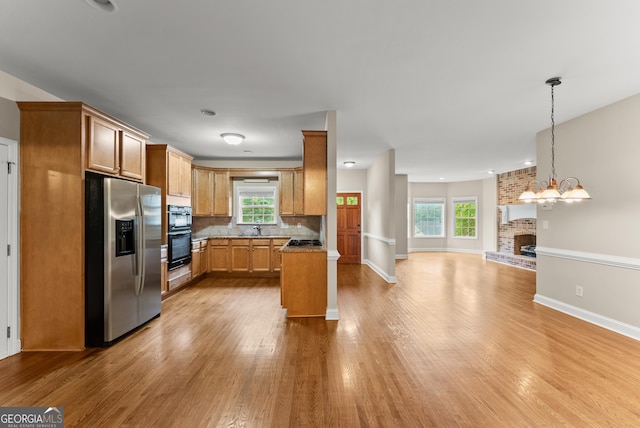 kitchen featuring a brick fireplace, pendant lighting, stainless steel appliances, light hardwood / wood-style flooring, and a notable chandelier