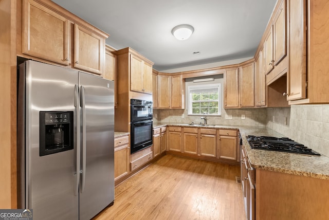 kitchen featuring tasteful backsplash, light stone countertops, stainless steel appliances, light wood-type flooring, and sink