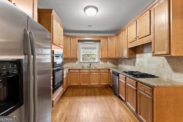 kitchen featuring light wood-type flooring, light stone counters, sink, decorative backsplash, and black appliances