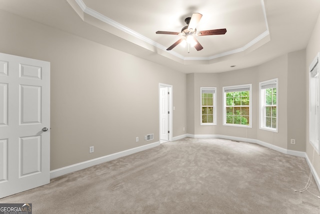 spare room with ceiling fan, light colored carpet, a tray ceiling, and crown molding