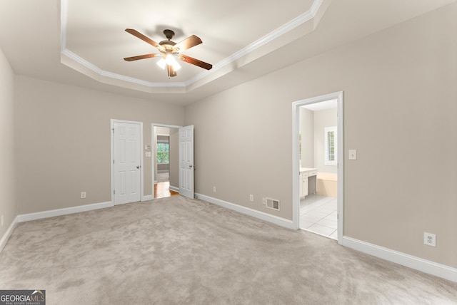 unfurnished bedroom featuring ceiling fan, a raised ceiling, ensuite bathroom, and multiple windows