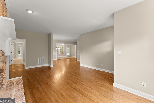 unfurnished living room with a brick fireplace, a chandelier, and light hardwood / wood-style floors