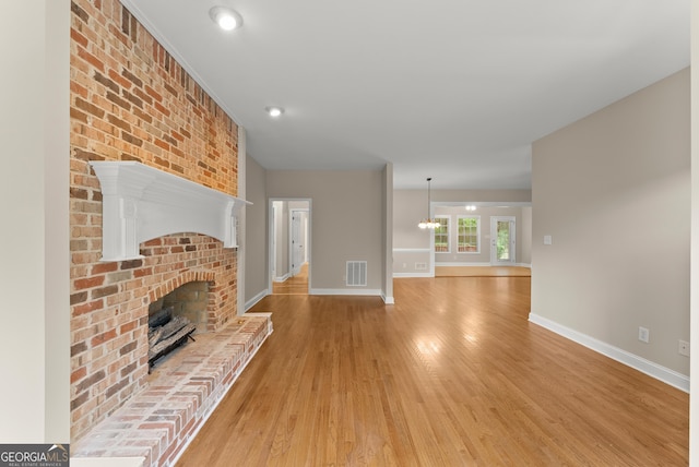 unfurnished living room featuring a brick fireplace, an inviting chandelier, and light wood-type flooring