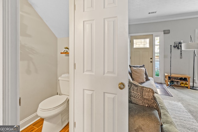 bathroom with toilet, a textured ceiling, hardwood / wood-style floors, and vaulted ceiling