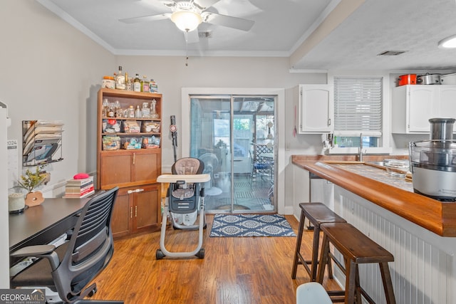 kitchen with a kitchen breakfast bar, crown molding, white cabinets, light hardwood / wood-style floors, and ceiling fan