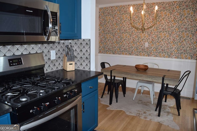 kitchen with blue cabinetry, stainless steel appliances, light wood-type flooring, and a chandelier