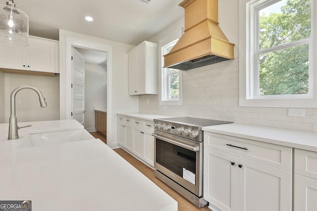 kitchen featuring premium range hood, white cabinetry, stainless steel range with electric cooktop, and hanging light fixtures