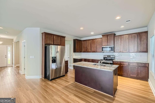 kitchen featuring light stone counters, an island with sink, sink, light hardwood / wood-style flooring, and appliances with stainless steel finishes