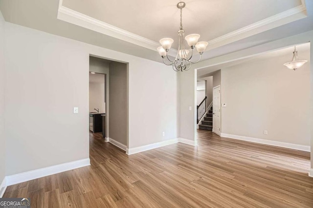 spare room with a raised ceiling, crown molding, an inviting chandelier, and hardwood / wood-style flooring