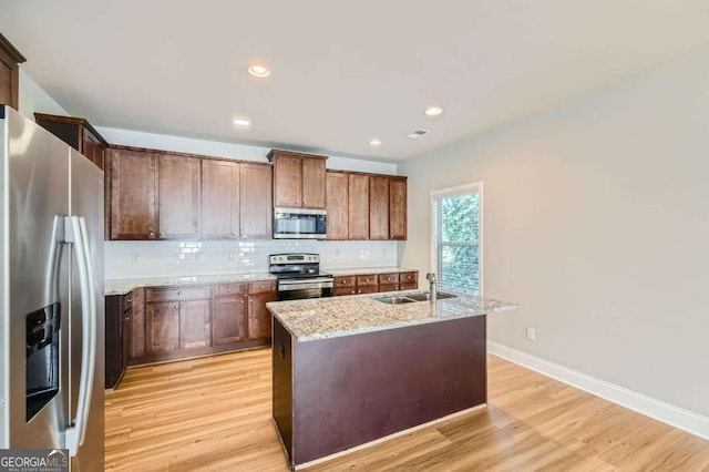 kitchen featuring light stone counters, stainless steel appliances, light hardwood / wood-style flooring, a kitchen island with sink, and sink